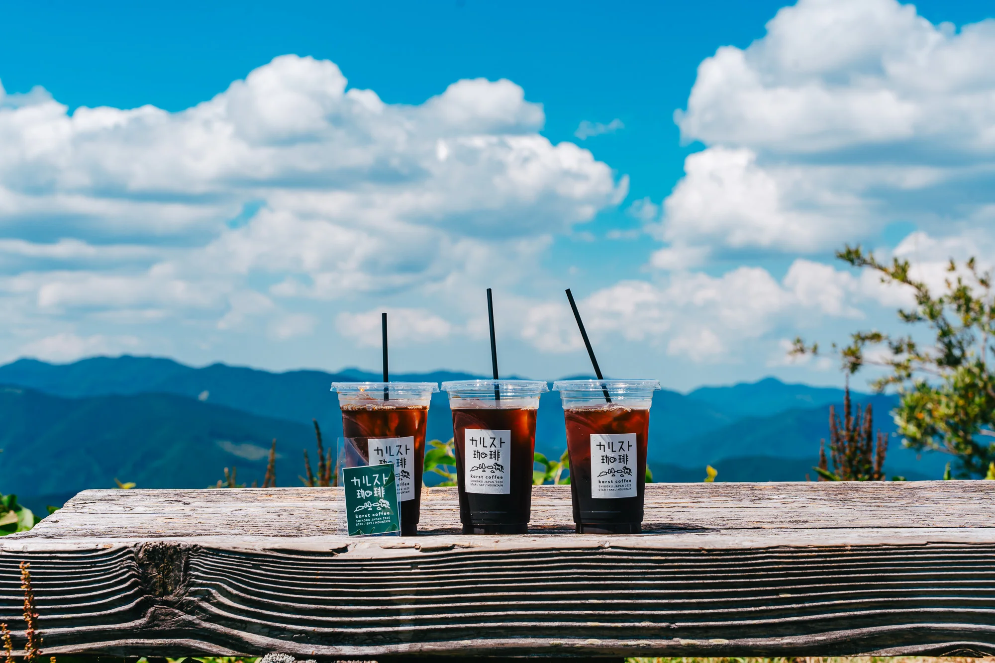 木の柵に置かれたカルスト珈琲のアイスコーヒー3杯と山の風景